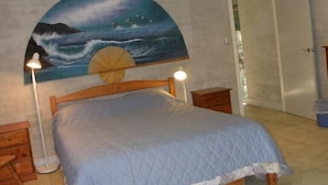 A bedroom with a bed, two bedside tables, a nightstand, a large painting of a seascape, and a door.