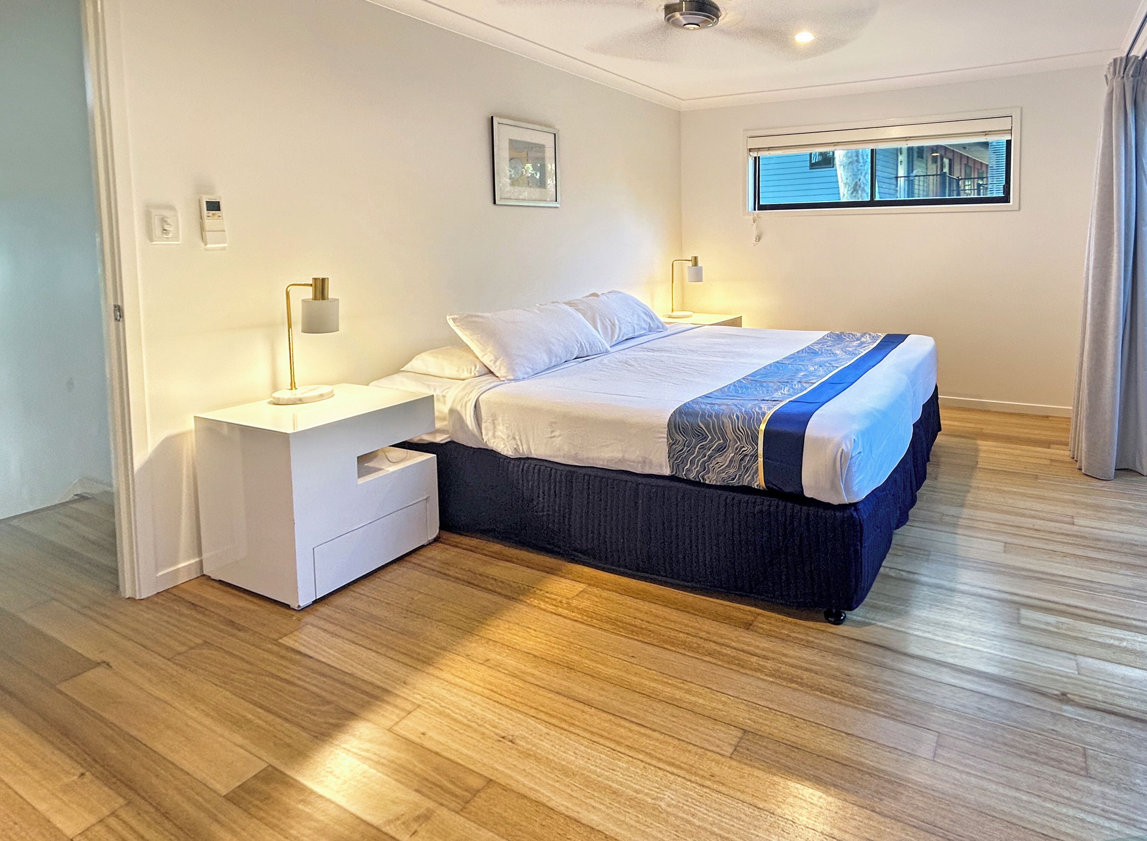 Une chambre à coucher avec un lit, des tables de chevet, une commode, une fenêtre et une vue sur l’extérieur.