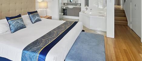 A modern hotel room with a large bed, a sitting area, a bathroom with a bathtub, and a staircase leading to another level.