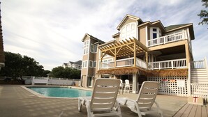 Une maison à deux étages avec une piscine, une terrasse en bois et un patio couvert.