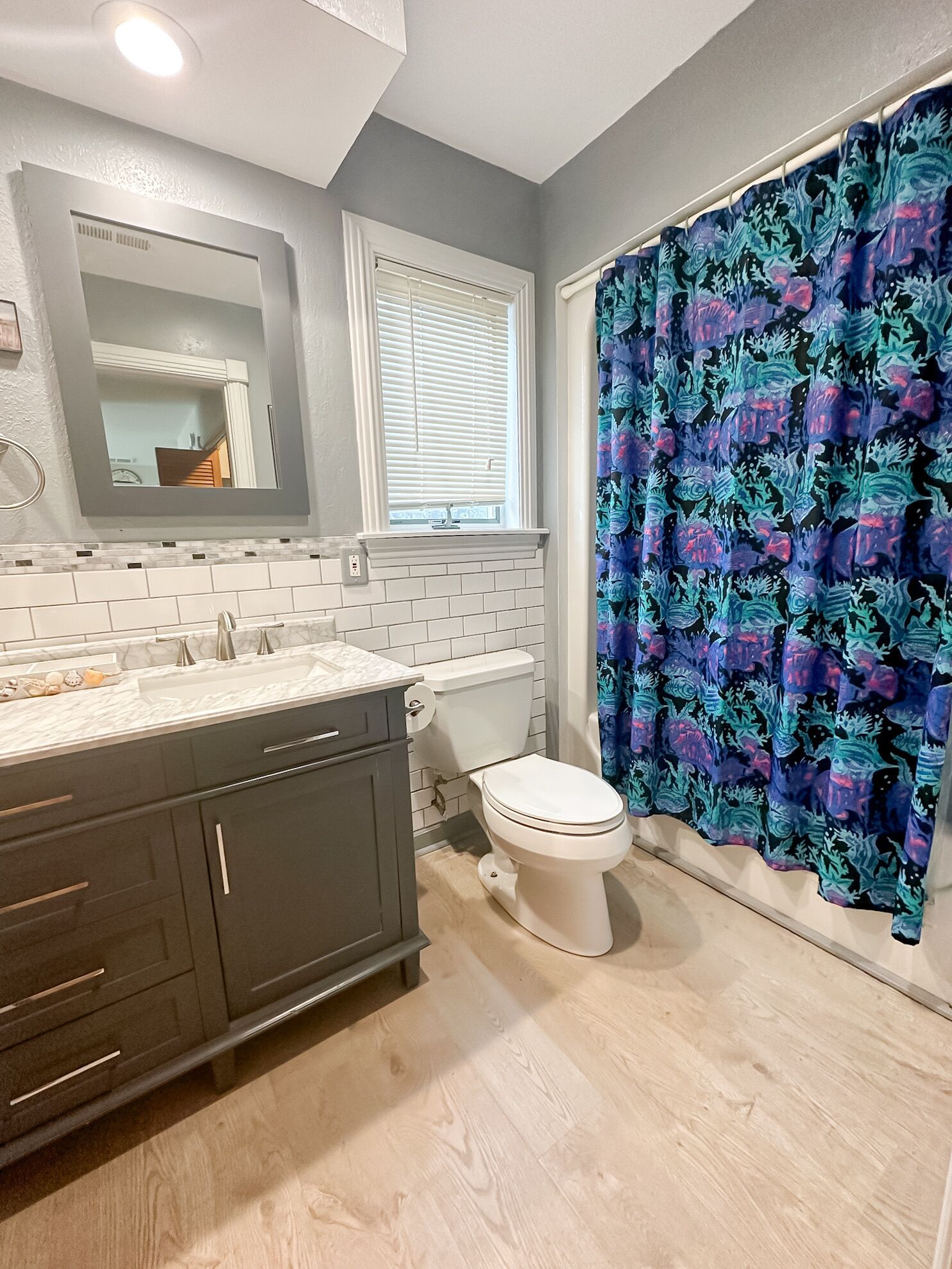 A bathroom with a white toilet, dark cabinets, a white sink, and a shower curtain with a blue and green pattern.