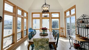 Une salle à manger avec un plafond haut, de grandes fenêtres et un lustre.