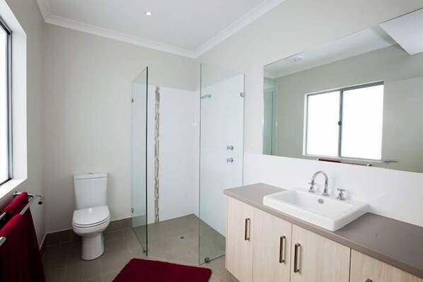 A modern bathroom with a glass shower enclosure, a white toilet, and a sink with a large mirror above it. - Views of Redwall Valley and close to beaches and wineries. (Yallingup)