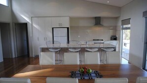 Cozinha moderna com armários brancos, uma ilha central com banquetas e uma mesa de jantar com cadeiras.