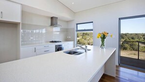 Cozinha moderna com uma ilha grande, eletrodomésticos de aço inoxidável e vista para o exterior.