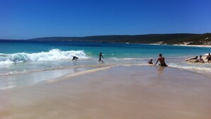 Uma praia com águas azuis cristalinas, areal arenoso e afloramentos rochosos ao fundo.
