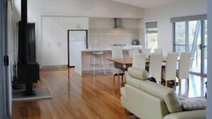 Uma sala de estar ampla, com pé direito alto, lareira, espaço para refeições e cozinha.
