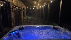 Un jacuzzi con luces LED azules, rodeado de muros de piedra y un área de patio techada con luces colgantes.