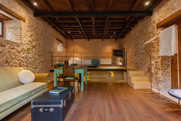 A rustic room with stone walls, wooden flooring, a sofa, a table, and a suitcase. - History and Charm in Old Town Chania (Chania)