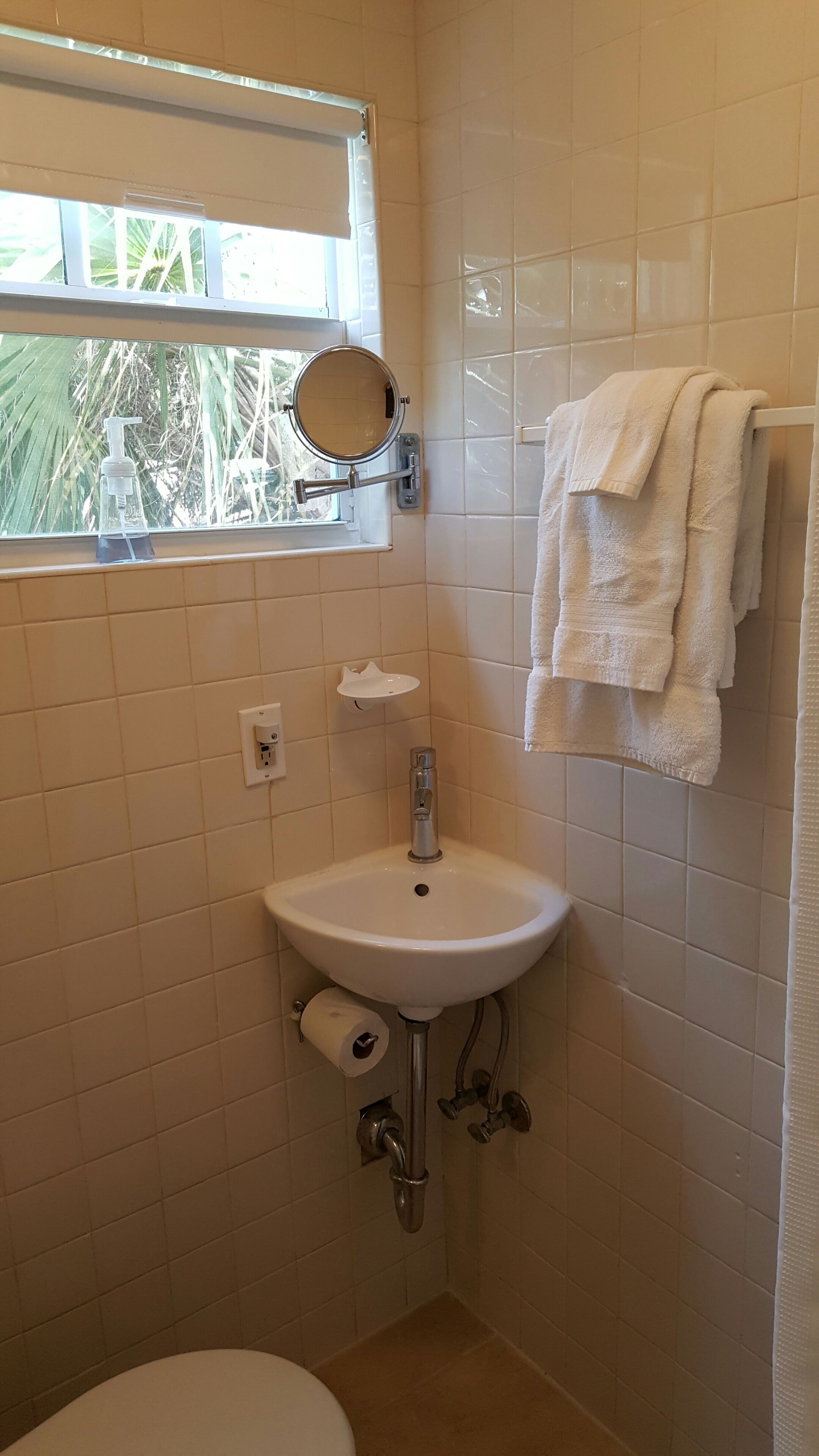 A bathroom with a white sink, a mirror, a window, and a towel rack.