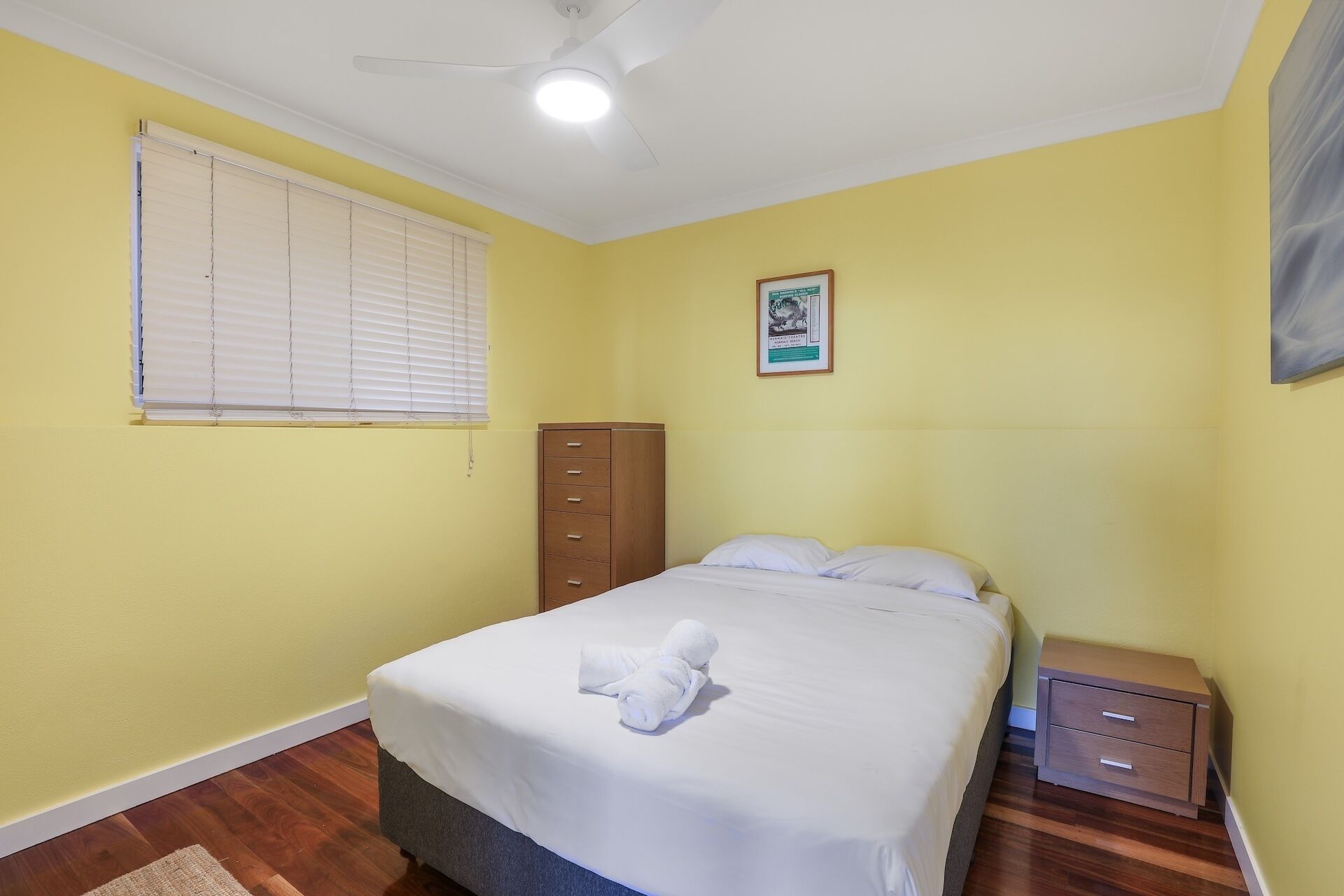 A bedroom with a bed, a nightstand, a wardrobe, a ceiling fan, and a window with blinds.