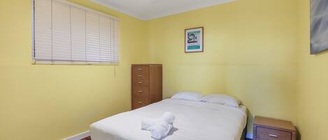 A bedroom with a bed, a nightstand, a wardrobe, a ceiling fan, and a window with blinds.