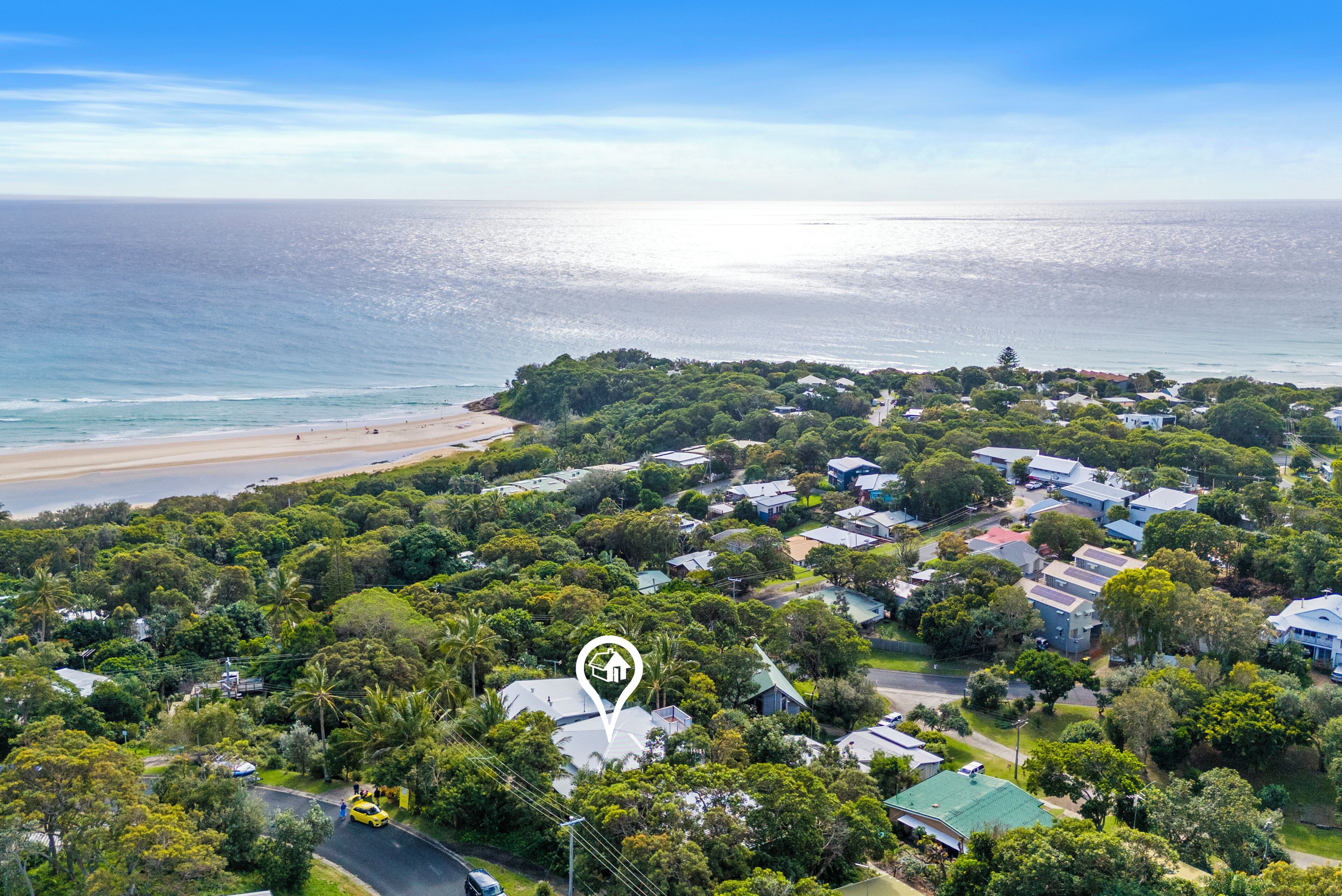 An aerial view of a coastal residential area with houses, a beach, and a dense green landscape.