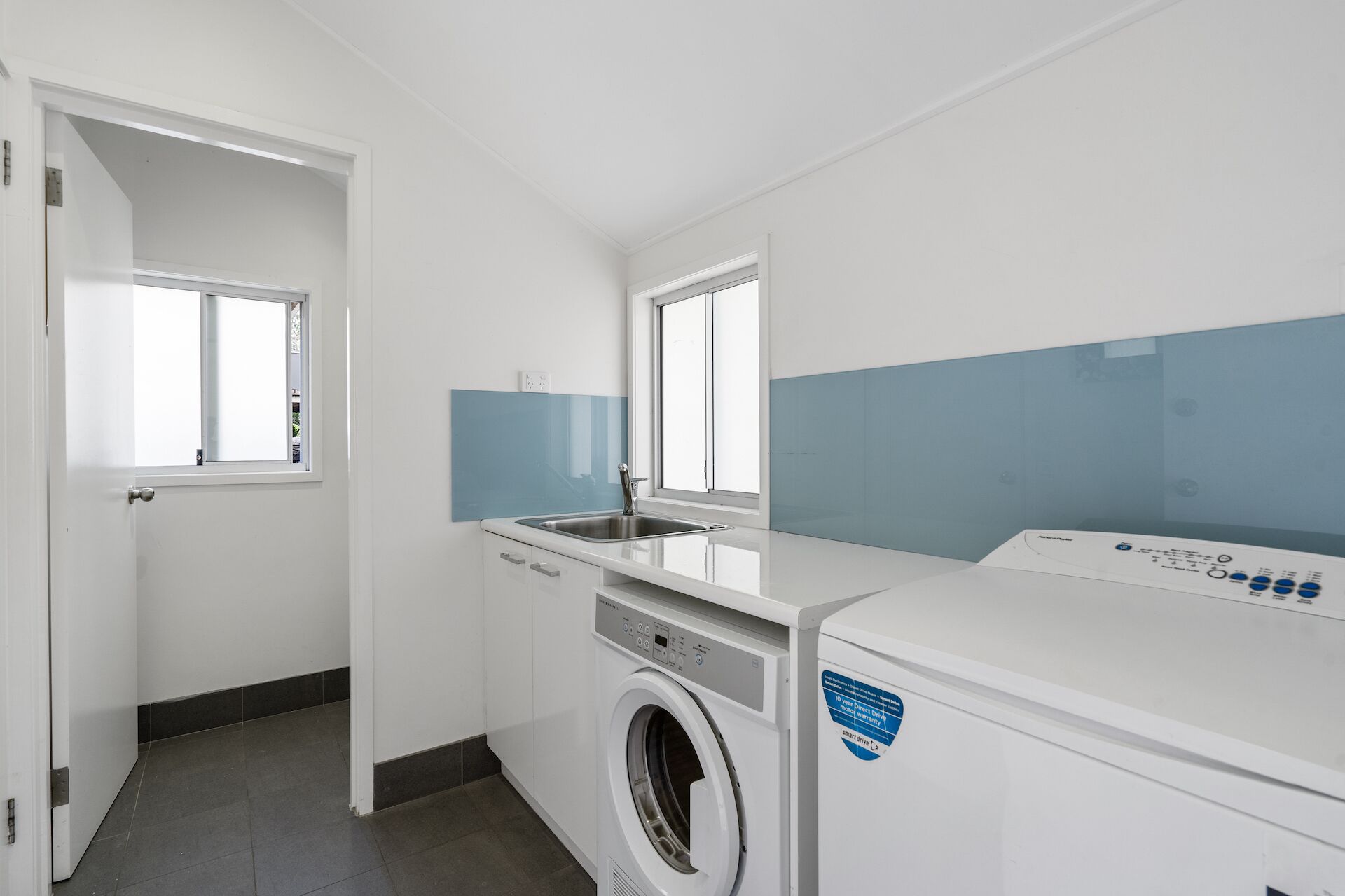 A laundry room with a washing machine, a sink, and a window.
