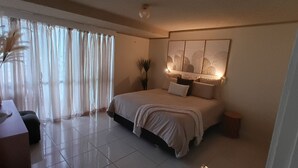 A bedroom with a bed, a desk, and a chair. There is a window with curtains and a plant. - Lowanna Unit 10, 24 Bulcock Beach Esplanade, Bulcock Beach (CALOUNDRA)