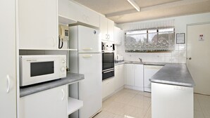 A compact kitchen with white cabinetry, a microwave, an oven, and a sink. - Lowanna Unit 10, 24 Bulcock Beach Esplanade, Bulcock Beach (CALOUNDRA)