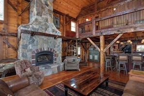 A rustic interior with a stone fireplace, wooden beams, a bar area, and a seating arrangement.