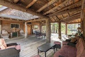 A rustic cabin with a wooden deck, furnished with wicker furniture and a sofa. - Unique Post & Beam Cabin on Winnipesaukee-  Mark Island-Gilford, NH (Gilford)