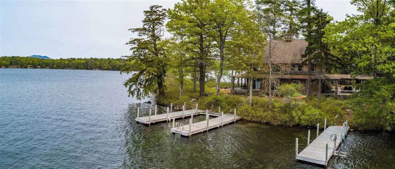 A lakeside cabin with dock access, surrounded by trees and a mountain in the background.