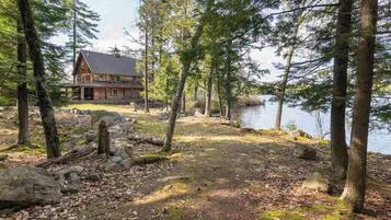 A cabin with a deck, surrounded by trees and a lake.