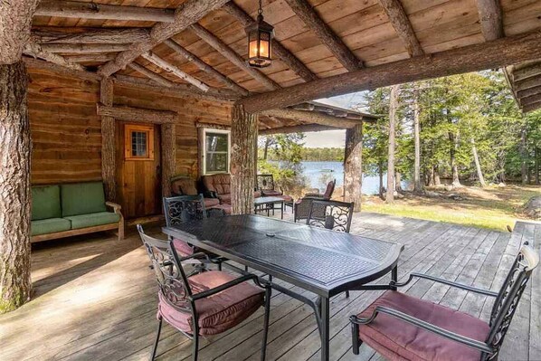 Un chalet rustique doté d’une terrasse en bois, d’une table à manger avec des chaises et offrant une vue sur un lac.