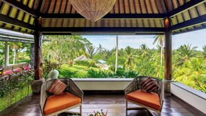 Un espace extérieur aménagé, abrité et doté de chaises en osier, offrant une vue sur un jardin luxuriant.