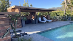 A swimming pool with a covered patio area, potted plants, and lounge chairs. - Langbrook Estate Cottage (Yarra Junction)