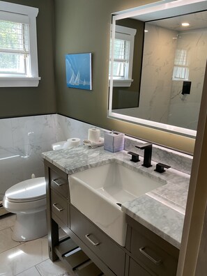 Un baño con inodoro blanco, lavabo con encimera de mármol y un espejo grande.