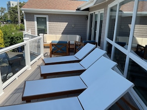 Una terraza con sillas reclinables blancas y una mesa de madera con cojines azules.