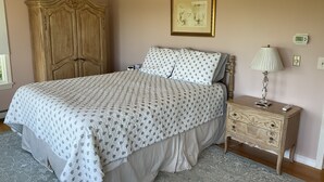 Una camera da letto con un letto, un comodino, una lampada, un armadio, un quadro appeso alla parete e un termostato.