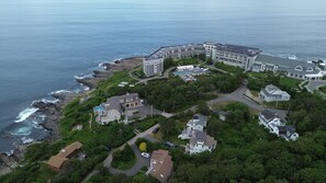 Une vue aérienne d’un quartier résidentiel situé sur la côte, avec de nombreux bâtiments, dont un grand hôtel doté d’une piscine et une maison plus petite avec un jardin.