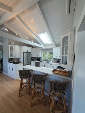 Une cuisine moderne avec des meubles blancs, un grand îlot central doté de tabourets et une verrière.
