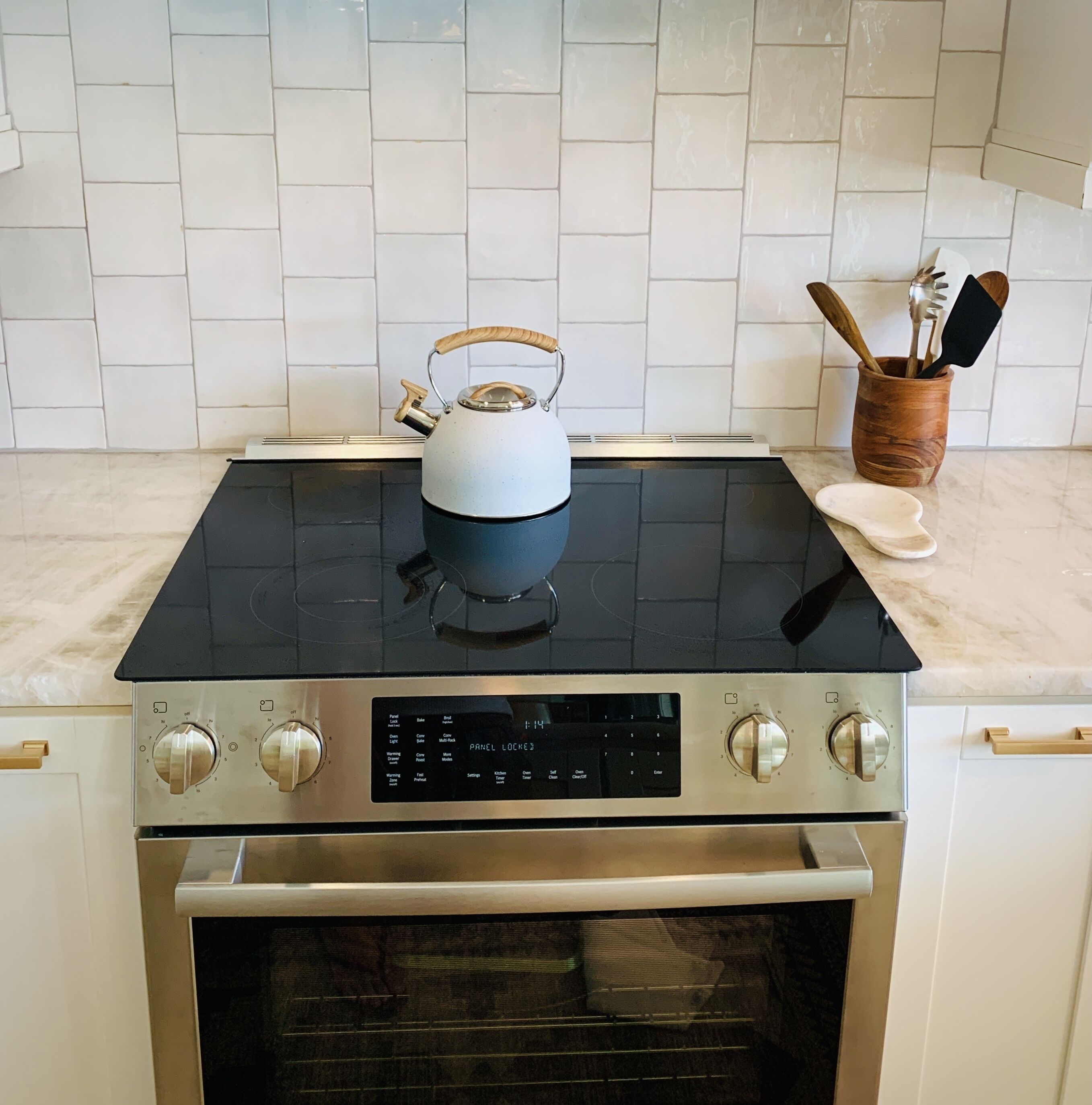 A kitchen with a black stovetop, a kettle, and a wooden utensil holder.