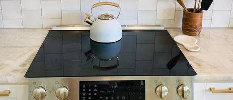 A kitchen with a black stovetop, a kettle, and a wooden utensil holder.