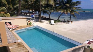 Une piscine entourée d’une terrasse en bois, de chaises longues et d’un panneau indiquant une zone « RÉSERVÉE AUX VACANCES ».