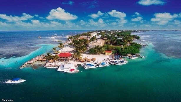 Vue aérienne d’une île tropicale avec une plage, des bateaux et une petite zone aménagée en station balnéaire.