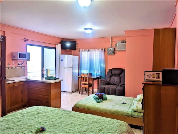 Une chambre avec deux lits, un bureau, une chaise, une télévision et un coin cuisine.