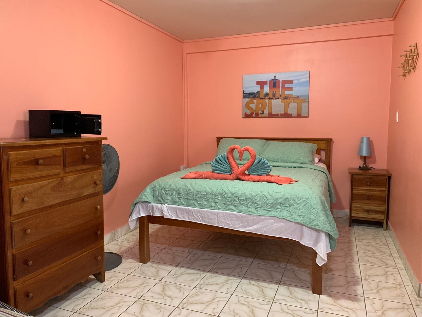 A bedroom with a bed, a dresser, a nightstand, a lamp, and a painting on the wall.