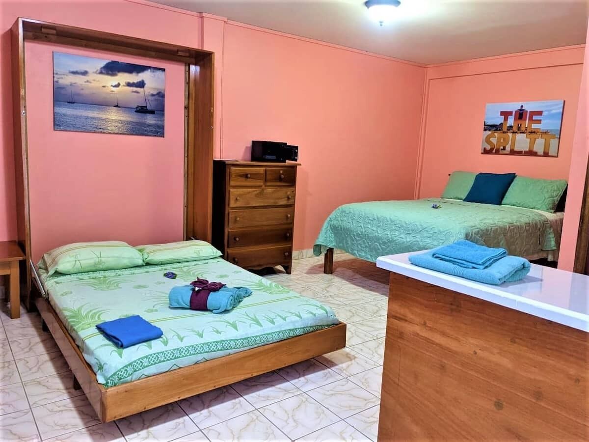 Ein Schlafzimmer mit zwei Betten, einer Holzkommode, einem Schreibtisch und einer Wand mit einem Gemälde und einem Schild.
