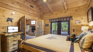 A wooden cabin interior with a bed, a television, and a fireplace.