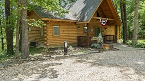 A log cabin with a porch, surrounded by trees.