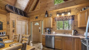 A wooden cabin kitchen with a dining area, wooden cabinets, a dishwasher, and a large window.