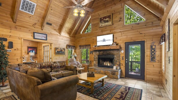 A cozy log cabin interior with a fireplace, wooden walls, and a large window.