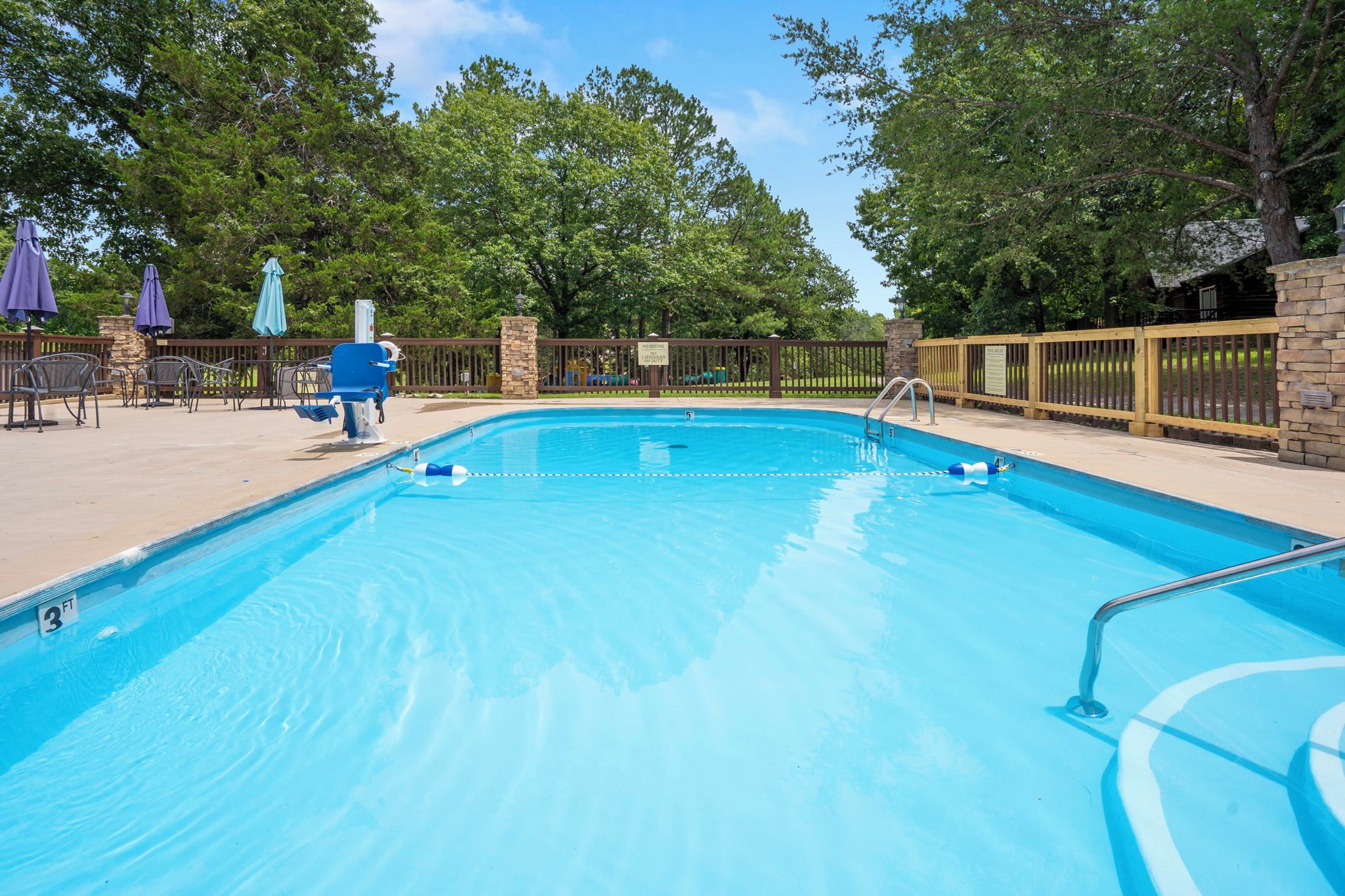 Ein klarer, blauer Pool mit einer Holzterrasse, Liegestühlen und Sonnenschirmen.