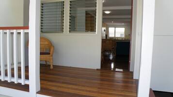 A wooden porch with a wicker chair, a glass door leading to a kitchen, and a staircase.