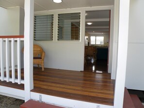 Un porche de madera con una silla de mimbre, una puerta de cristal que da a una cocina y una escalera.