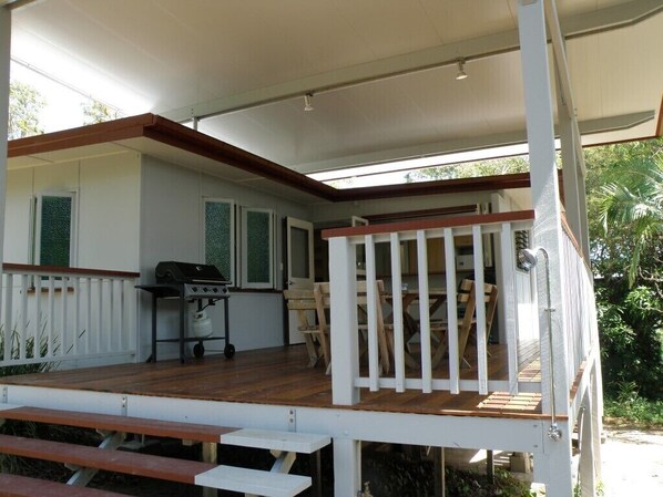 A covered outdoor deck with a grill, seating area, and a view of the surrounding greenery.