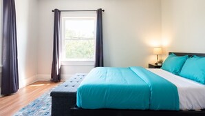 Un dormitorio con cama, mesita de noche, lámpara y ventana con cortinas.