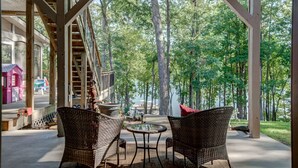 A covered outdoor seating area with wicker chairs and a small table, overlooking a forested area. - Pool, lake, hot tub, fishing, fun-Lake Lanier GA. Newly renovated and open again (Gainesville)