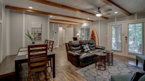 A spacious living room with a wooden ceiling, a leather sofa, a dining table with chairs, and a patterned rug. - Pool, lake, hot tub, fishing, fun-Lake Lanier GA. Newly renovated and open again (Gainesville)